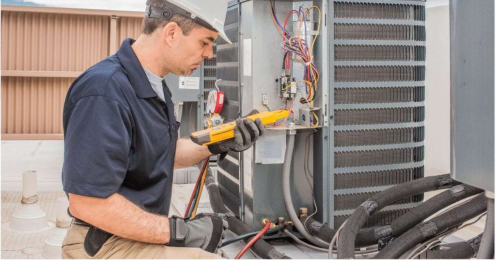 Image of a man wearing a hard hat and working on an outdoor HVAC unit.